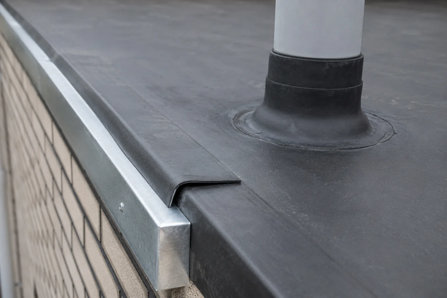 Verlijmde dakrand met metalen daktrim en een dakdoorvoer met rubberen manchet op een plat dak met EPDM